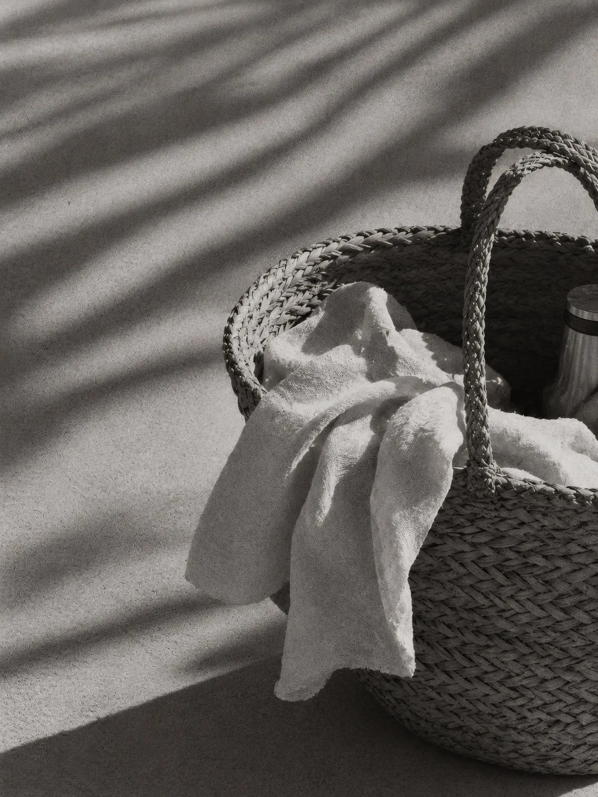 Black and white still life of a woven beach tote in palm shadows