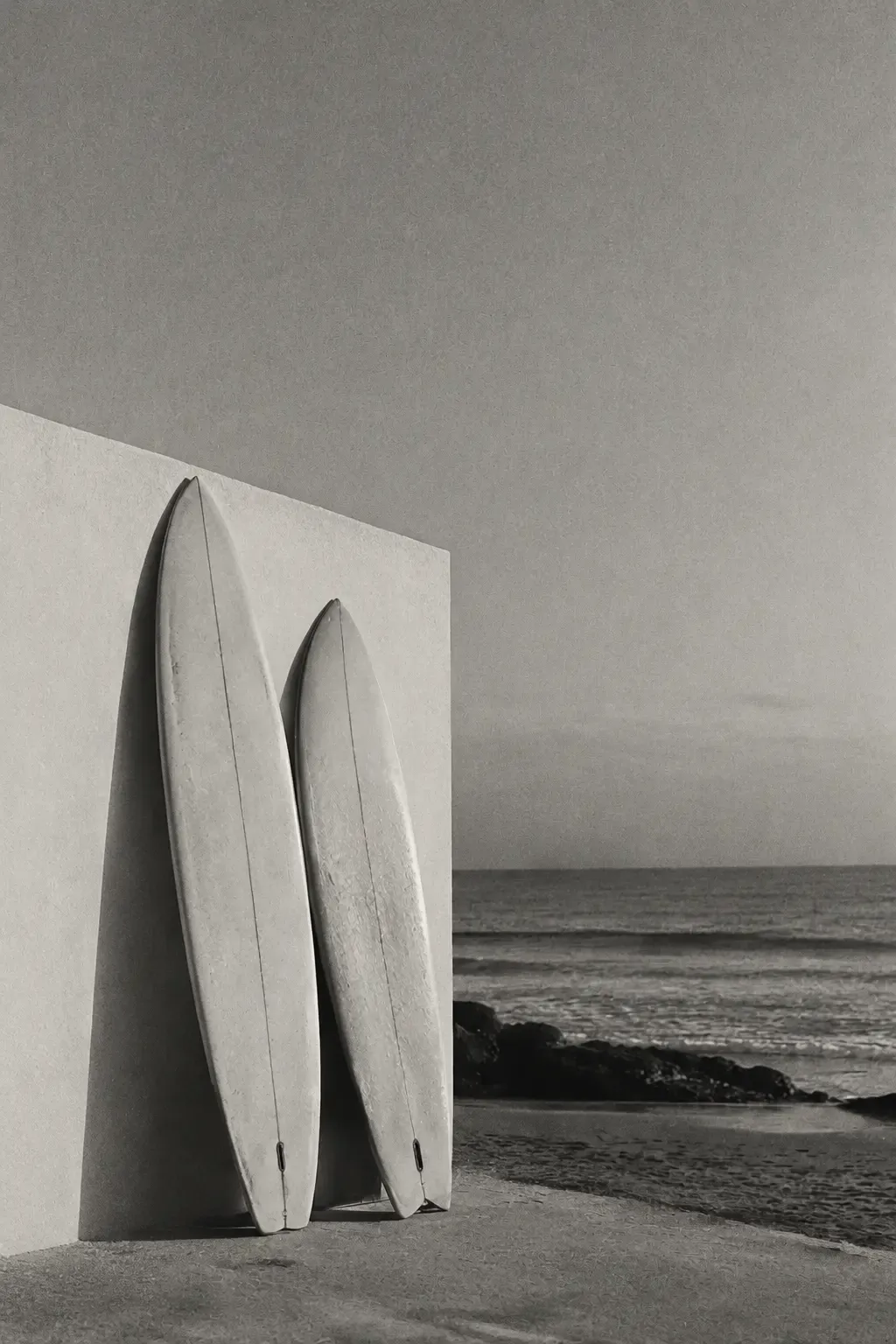 Two surfboards against a white wall by the sea, black and white