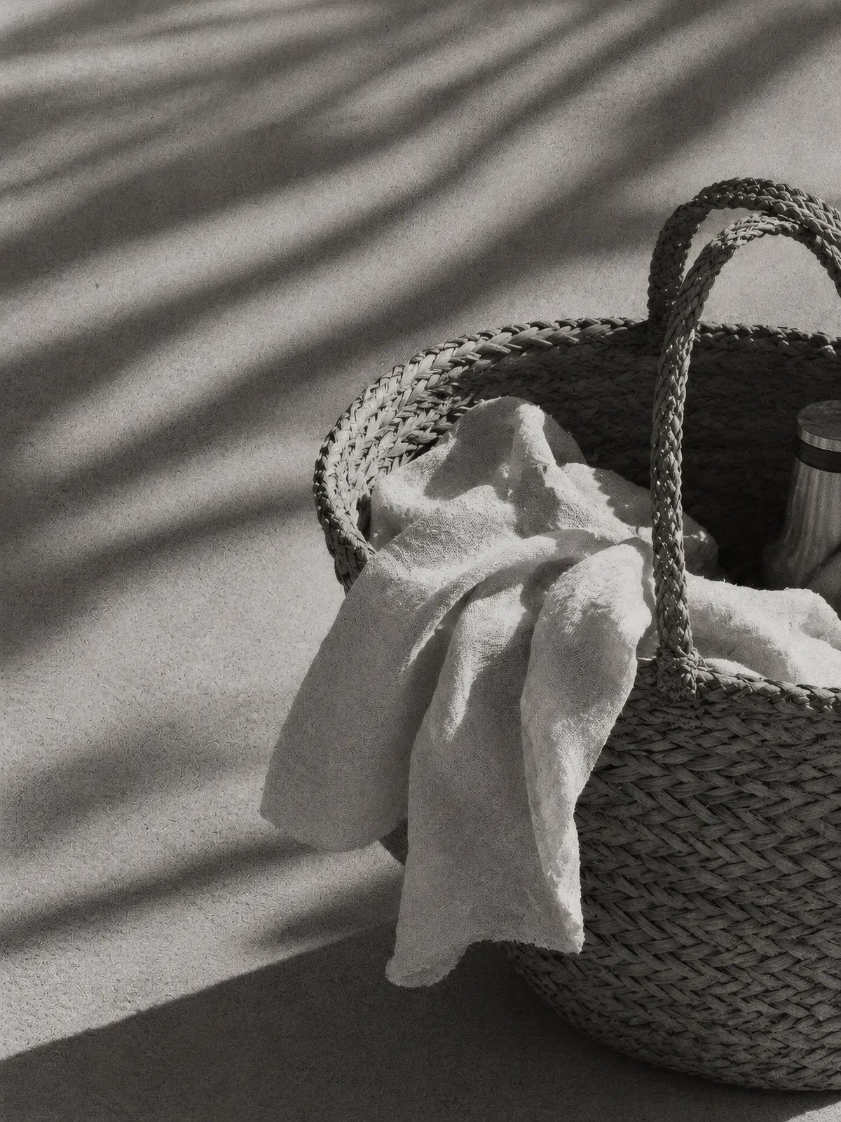 Woven beach tote with a linen towel under palm shadows